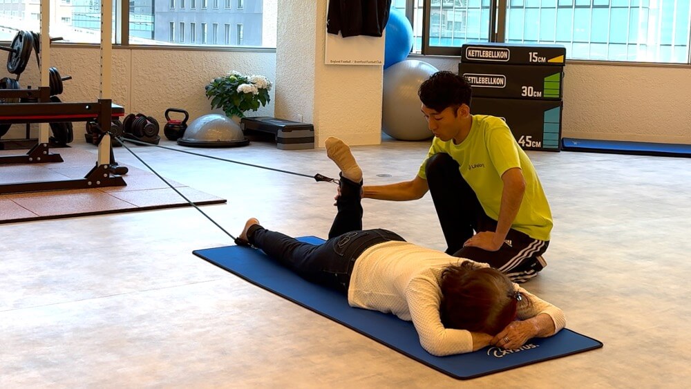 an elderly woman is performing leg curl with her physiotherapist.