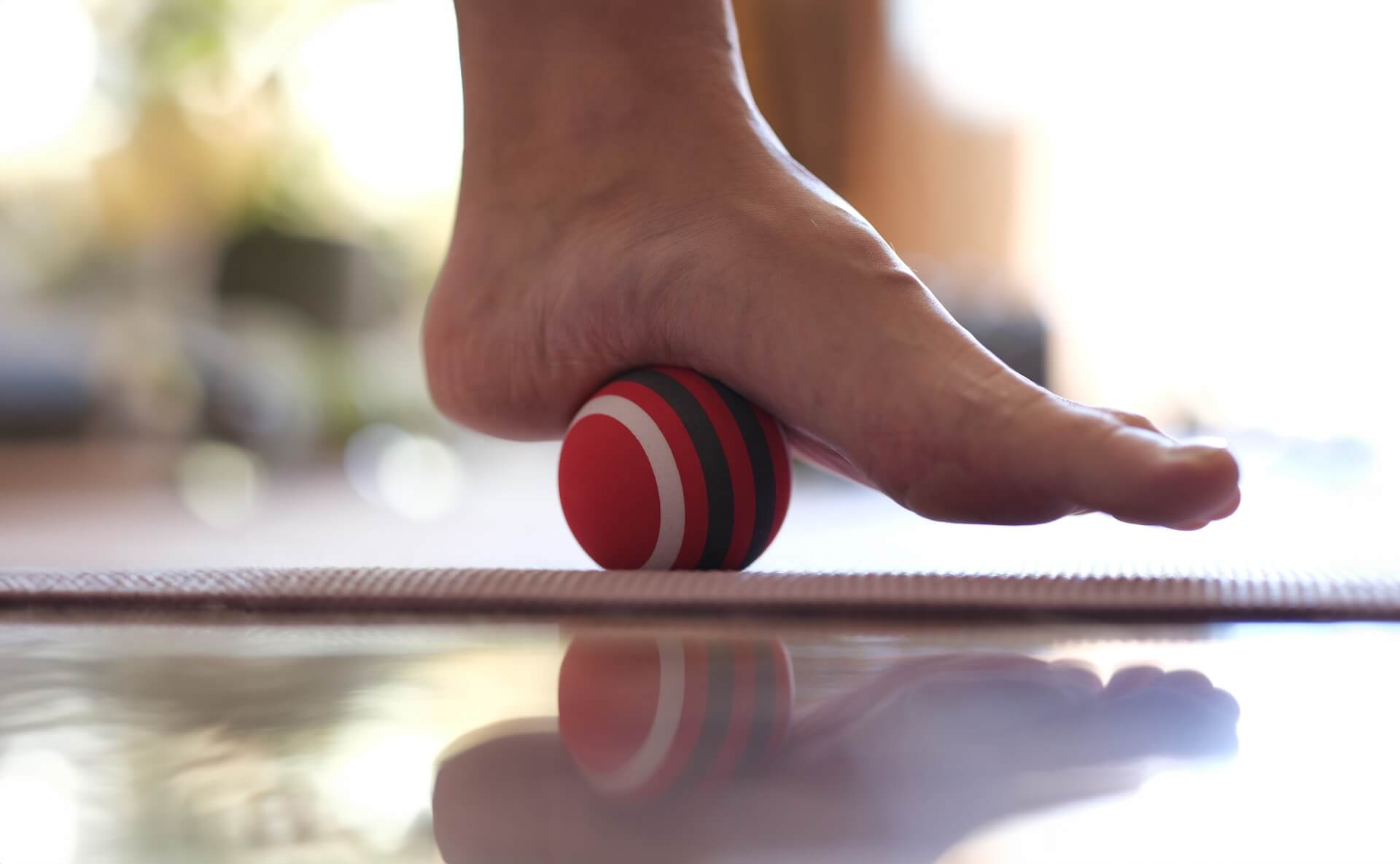 a women is releasing tension of her sole muscles by using a tennis ball to treat her plantar fasciitis.